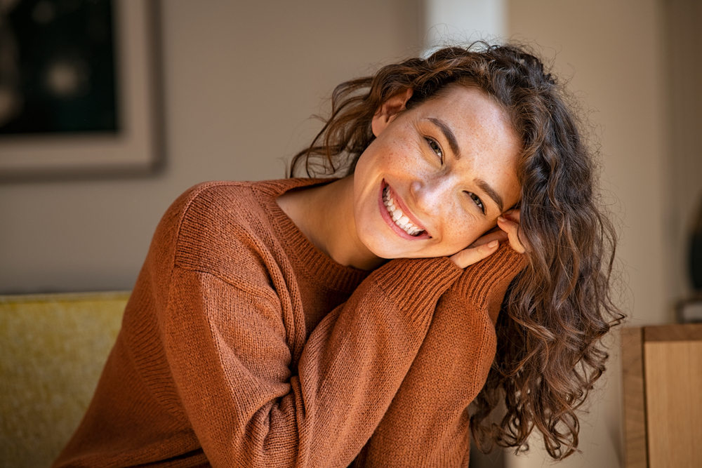 A curly-haired woman in a warm sweater smiling at the camera.