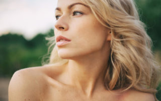 A blonde woman looking towards the left of the screen. Her nose is perfectly shaped. And she's sitting outside.