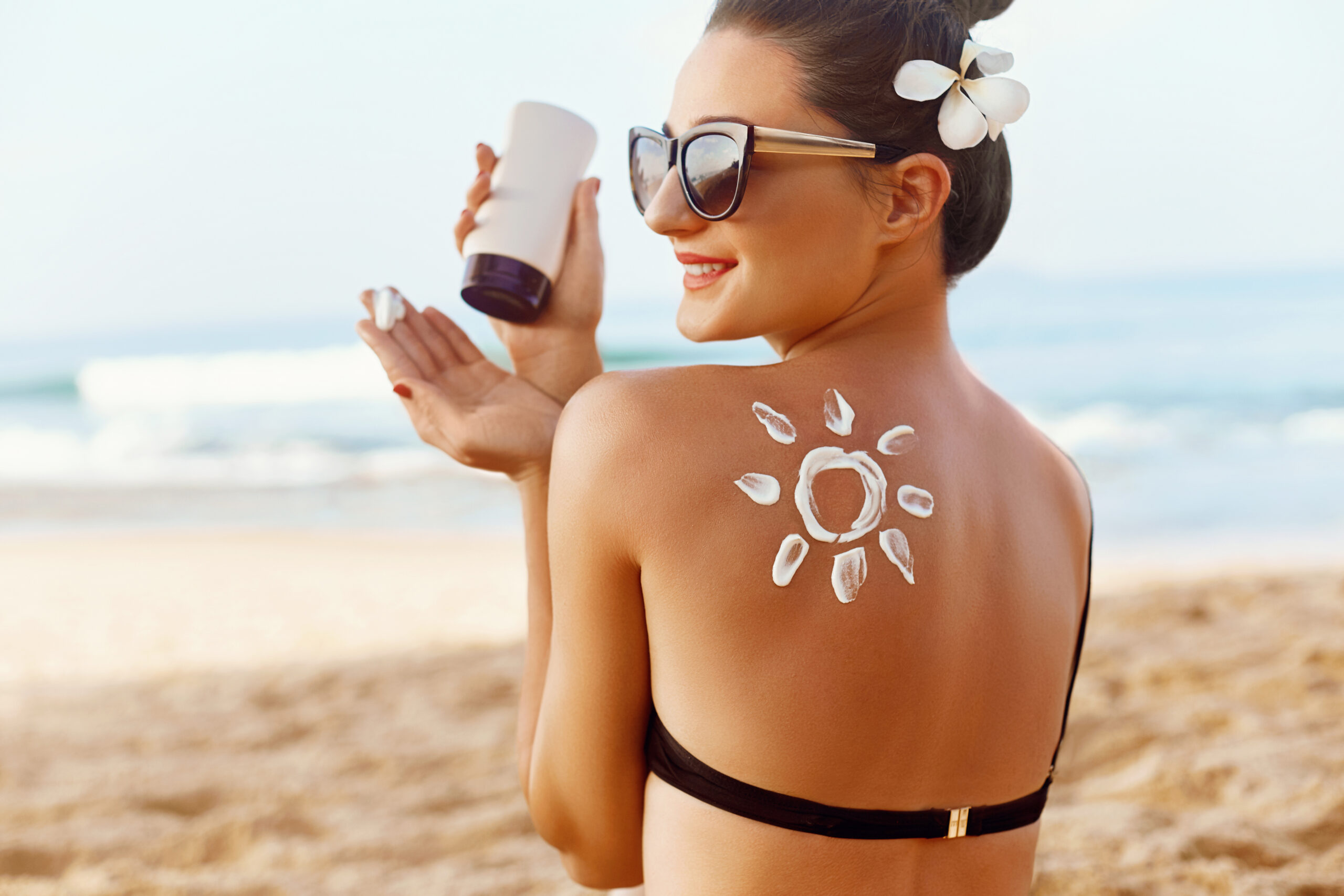 woman at the beach applying sunscreen to protect her skin and maintain the perfect bbl from garza plastic surgery in nashville