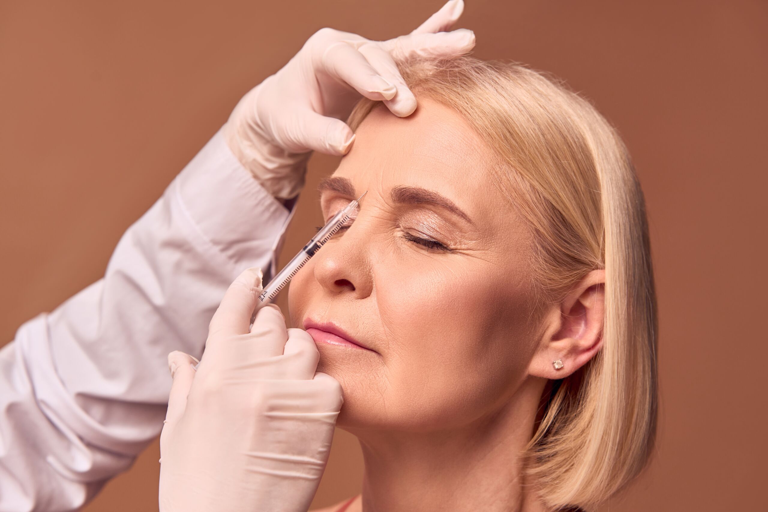 Older woman receiving botox/filler into 11 lines on forehead.