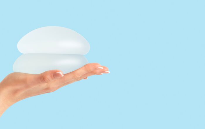 Hand holding breast implant device with blue background.