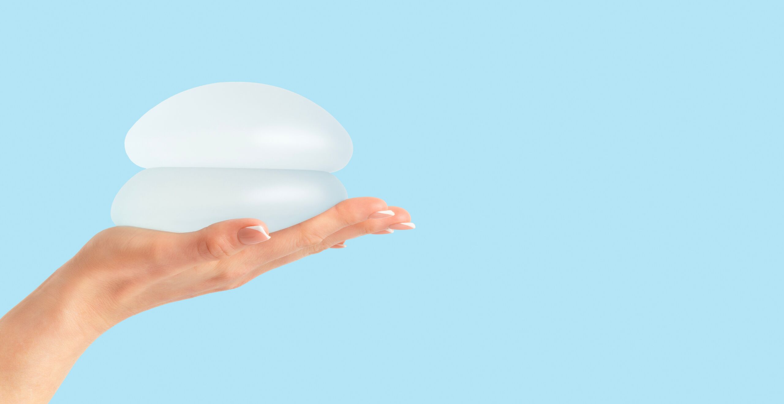 Hand holding breast implant device with blue background.